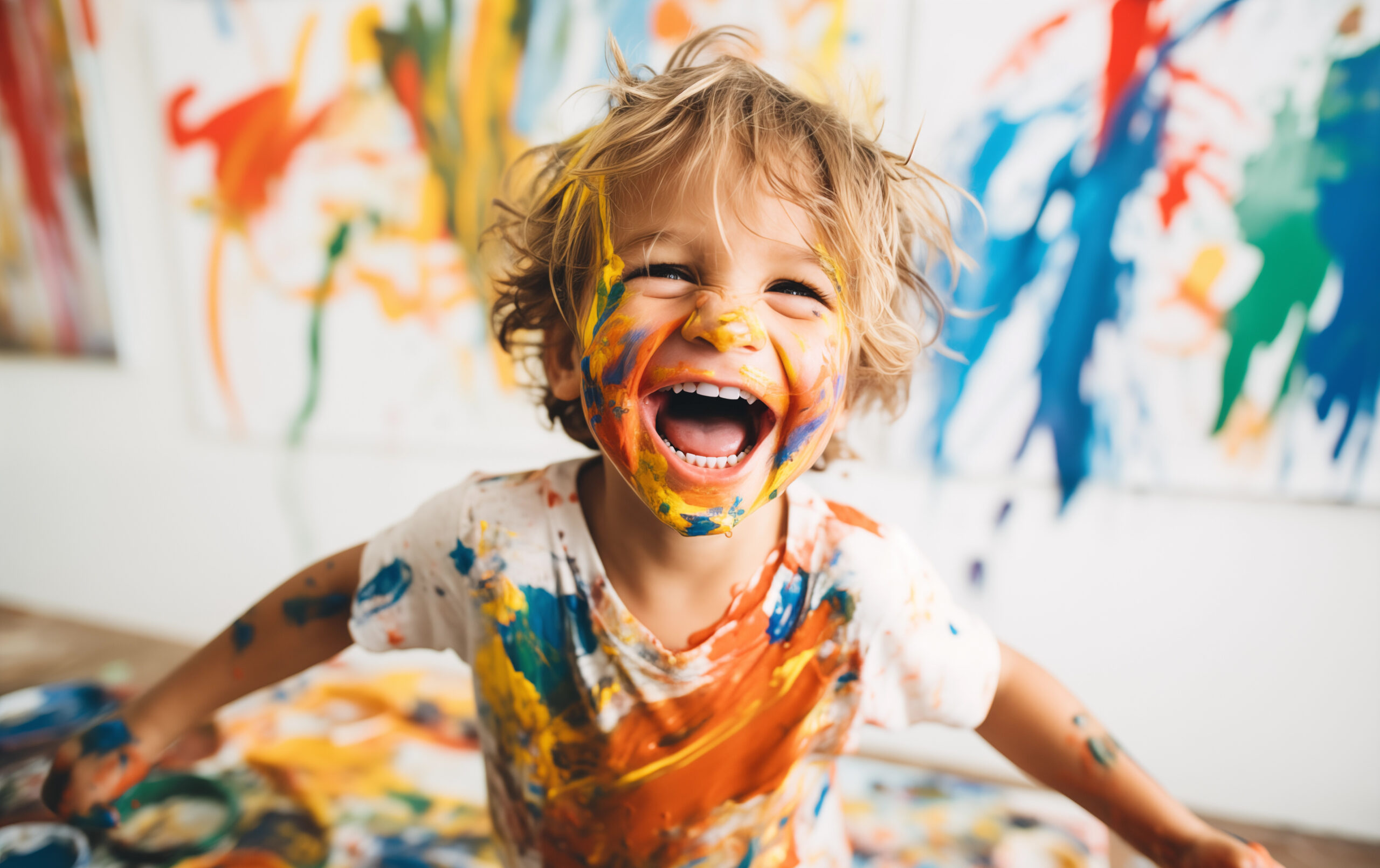 a young child is the epitome of joy and creativity, his face and clothes a canvas of vibrant paint splatters, against a backdrop of colorful artwork.